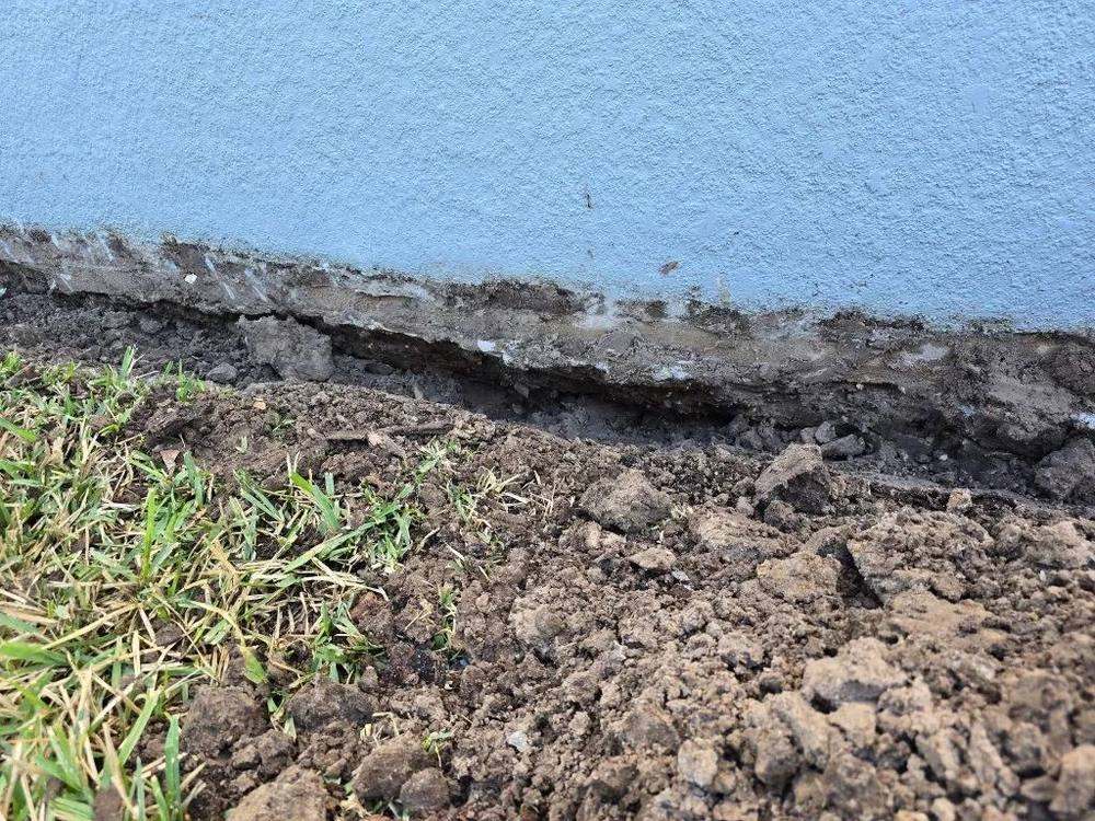 Soil eroded away along home foundation slab from roof runoff